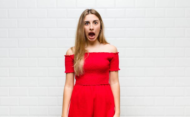 blonde woman feeling terrified and shocked, with mouth wide open in surprise - Fotó, kép