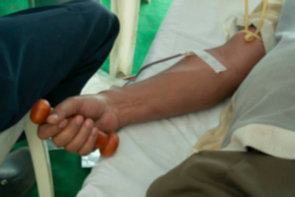 Rozmazaný obraz indiánského dobrovolníka držícího činku a darujícího krev v dárcovském táboře. Kalkata, Západní Bengálsko, Indie. - Fotografie, Obrázek