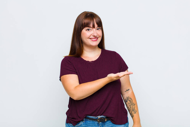 overweight woman smiling cheerfully, feeling happy and showing a concept in copy space with palm of hand - Photo, image