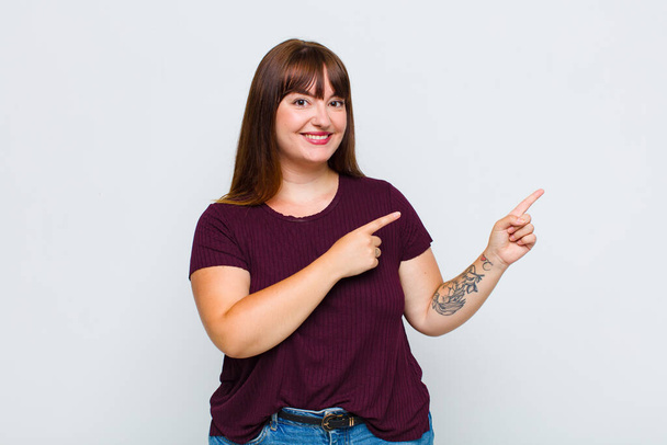 overweight woman smiling happily and pointing to side and upwards with both hands showing object in copy space - Foto, immagini