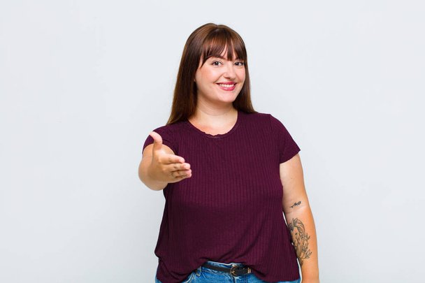 overweight woman smiling, looking happy, confident and friendly, offering a handshake to close a deal, cooperating - Фото, зображення