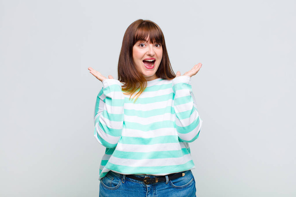 overweight woman looking happy and excited, shocked with an unexpected surprise with both hands open next to face - Photo, Image