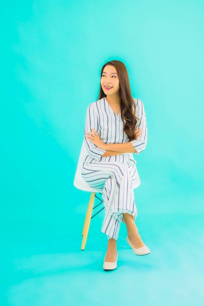 Portré gyönyörű fiatal ázsiai nő mosoly és ül széken kék elszigetelt háttér - Fotó, kép