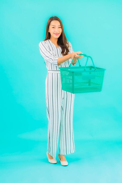 Porträt schöne junge asiatische Frau mit Einkaufskorb im Supermarkt auf blauem Hintergrund - Foto, Bild