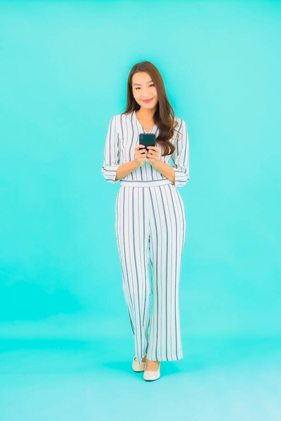 Retrato hermosa joven asiática mujer uso inteligente teléfono móvil sobre fondo azul - Foto, imagen