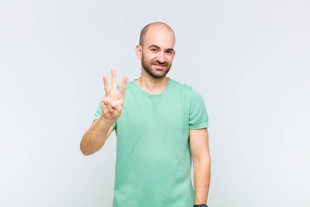 bald man smiling and looking friendly, showing number three or third with hand forward, counting down - Foto, Imagen