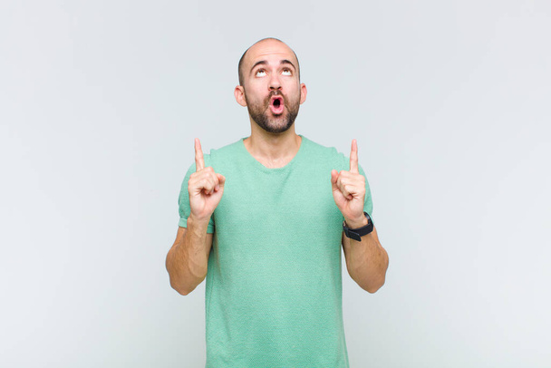 bald man looking shocked, amazed and open mouthed, pointing upwards with both hands to copy space - Foto, imagen