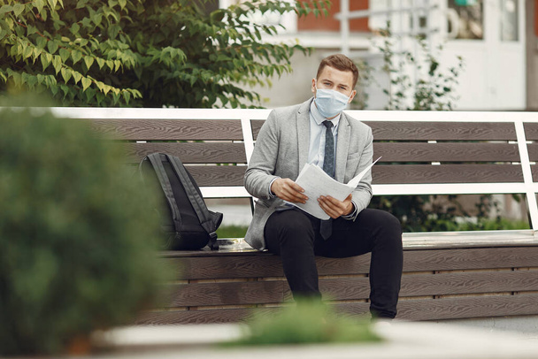 Businessman in a mask sitting on a bench with documents - Foto, Imagem