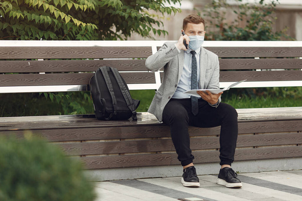 Businessman in a mask sitting on a bench with documents - Photo, Image