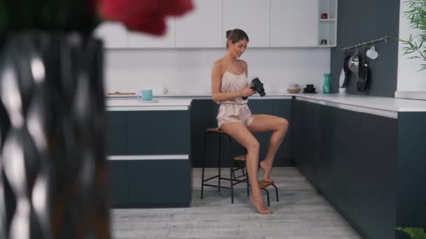 girl uses a body massager while sitting in the kitchen - Video, Çekim