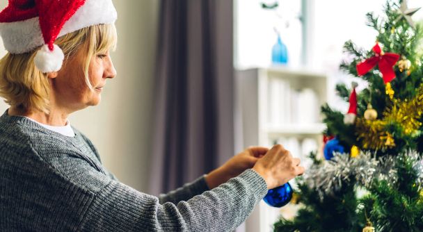 Žena v Santa klobouky baví zdobení vánoční stromeček a usmívá se při oslavě Silvestr a užívat si trávení času spolu ve vánočním čase doma - Fotografie, Obrázek