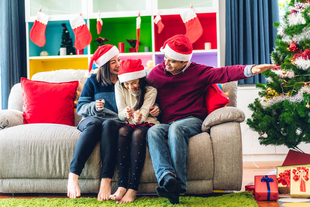 Ritratto di felice famiglia asiatica padre e madre con figlia in cappelli di Babbo Natale divertirsi guardare la macchina fotografica e godersi il tempo trascorso insieme nel tempo di Natale a casa - Foto, immagini
