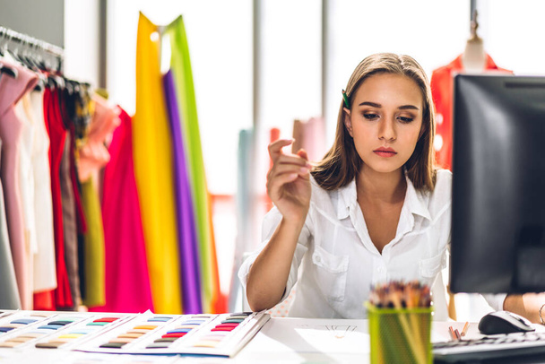 Portrait of young beautiful pretty woman fashion designer stylish sitting and working.Attractive young girl use desktop conputer and colorful fabrics at fashion design studio - 写真・画像