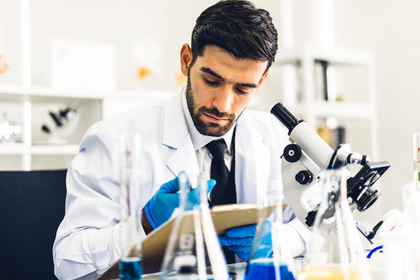 Ammattimainen tiedemies mies tutkimus ja työskentely tekee kemiallisen kokeen samalla analysoimalla ja sekoittamalla nestettä koeputkessa. - Valokuva, kuva