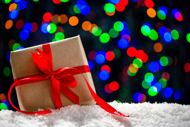 Christmas gift in snow on blurred lights background. - Valokuva, kuva
