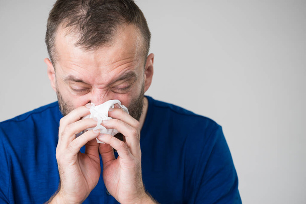 Man having flu, sneezing into hygienic tissue. Guy being sick, allergic blowing his nose. - Фото, изображение
