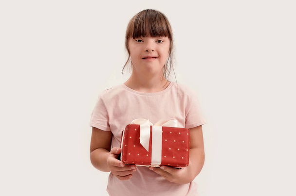 Portrait of disabled girl with Down syndrome smiling at camera, holding birthday present while posing isolated over white background - Photo, Image