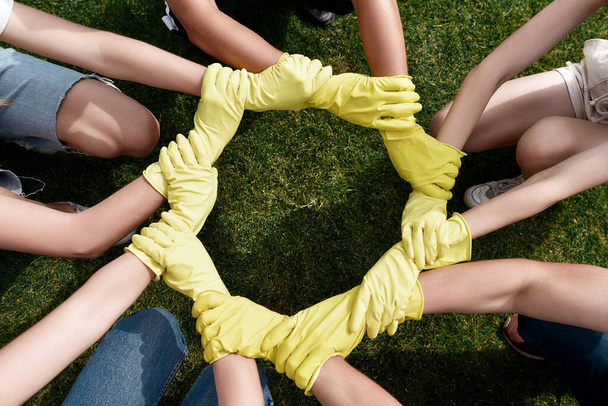 Great teamwork. Group of volunteers wearing protective rubber gloves putting their hands together while cleaning up a park - 写真・画像