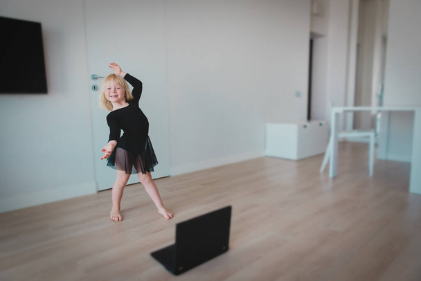 Ballet lesson online. Little girl dancing while looking at computer at home. - Photo, Image