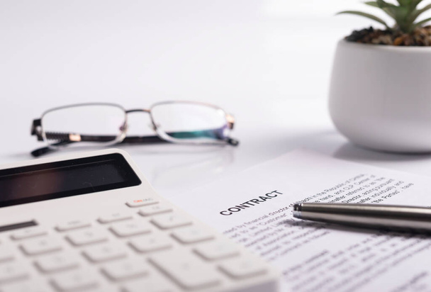 Office desk or table with contract paper, documents, calculator, potted plant, pen and eyeglasses. Close up of business workplace - Фото, изображение