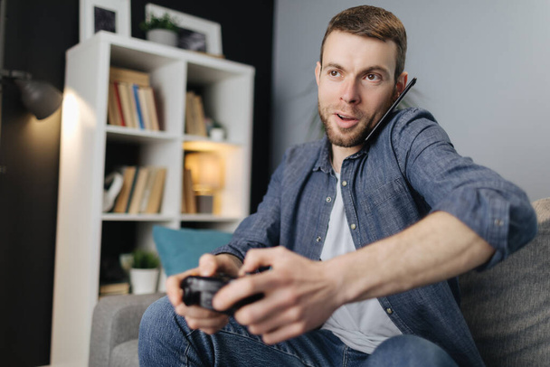 Man praten op mobiel tijdens het spelen van videospelletjes - Foto, afbeelding