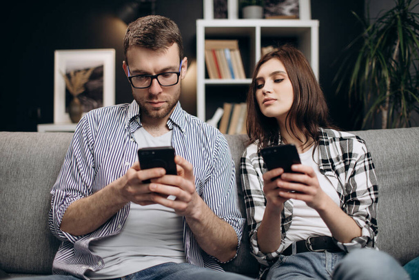 Молодий чоловік і жінка використовують смартфони вдома
 - Фото, зображення