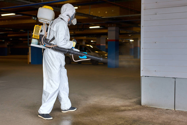 professional worker in hazmat suit is making disinfection outdoors - Photo, image
