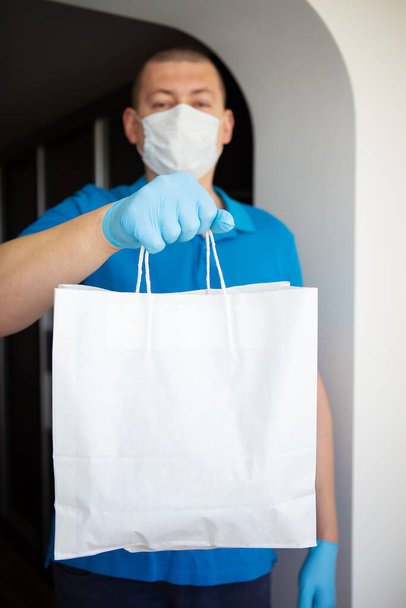 Contactless delivery in mask and disposable gloves of a package with products. Concept of quarantine and isolation during a coronavirus pandemic. Close-up. - Photo, Image