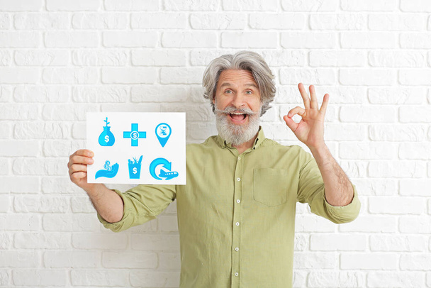 gelukkig bejaarde man schaaft zijn budget op wit baksteen achtergrond - Foto, afbeelding