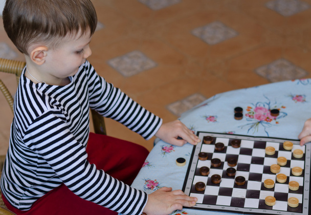 kleine jongen een game van checkers instellen - Foto, afbeelding