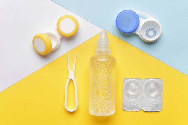 Containers with contact lenses, solution and tweezers on color background - Photo, Image