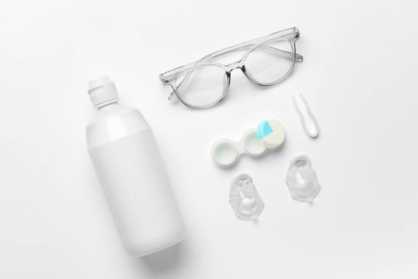 Container with contact lenses, solution, tweezers and eyeglasses on white background - Photo, Image