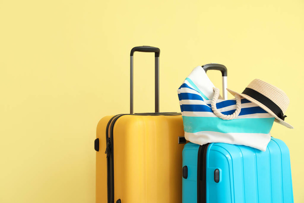 Упакованные чемоданы с пляжной сумкой и шляпой возле цветной стены - Фото, изображение
