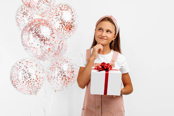 Pensive beautiful little girl child, holding balloons and gift box, on isolated white background - Foto, Imagem