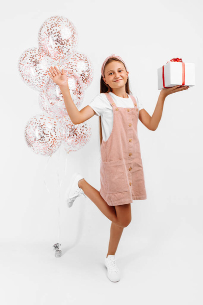 Adorable excited little girl with balloons and a gift, on an isolated white background, The concept of a holiday, Birthday - Φωτογραφία, εικόνα