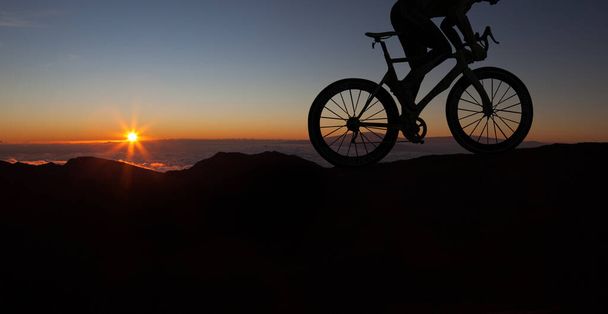 Pyöräilijän siluetti pyörällä auringonlaskun aikana.Mies ajaa pyörällä vuorilla. Urheilu ja aktiivinen elämä käsite auringonlaskun aikaa. Mies ajaa polkupyörällä luonnossa. - Valokuva, kuva