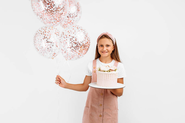Beautiful happy little girl holding a beautiful big birthday cake, birthday celebration with balloons, over isolated white background - 写真・画像
