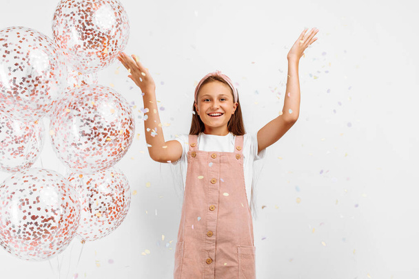 Happy excited little girl celebrating and exploding up colorful confetti, over isolated white background - Fotó, kép
