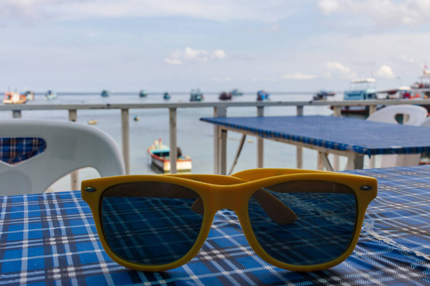 タイ島の海のレストラン、。青いテーブルの屋外家具に滞在黄色のフレームサングラス - 写真・画像