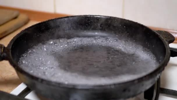 Verter agua de vidrio en una sartén caliente y grasosa. Líquido hirviendo, evaporación - Imágenes, Vídeo
