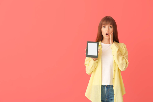 Mujer joven sorprendida con e-reader sobre fondo de color - Foto, Imagen