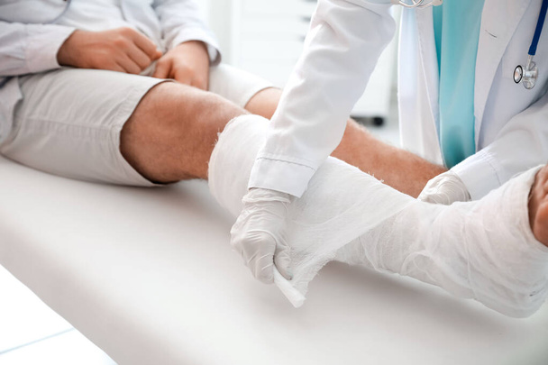 Doctor poniendo pierna rota de joven en yeso - Foto, imagen