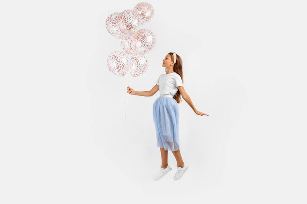 Excited funny young girl jumping high celebrating and holding colorful balloons isolated on white background. Birthday party - Fotó, kép