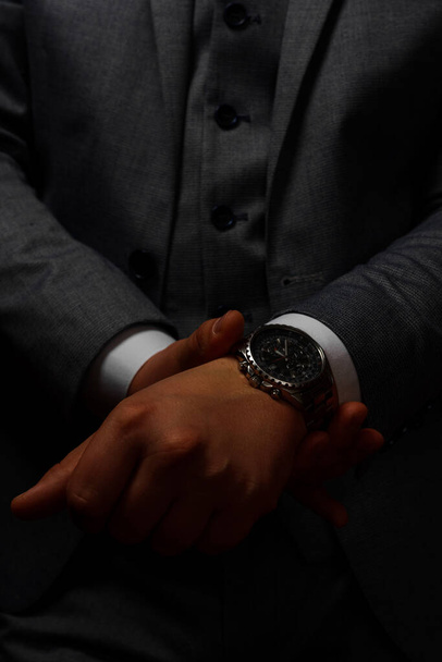 manos masculinas se cierran, el novio se prepara en la mañana antes de la ceremonia de la boda. El hombre ajusta un reloj en su mano sobre un fondo oscuro 2021. - Foto, imagen