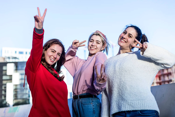 Front view of three young Teenage girls making a peace sign outdoors in a sunny day - 写真・画像