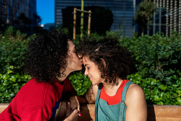 Smiling lesbian couple embracing and relaxing on a park bench - 写真・画像