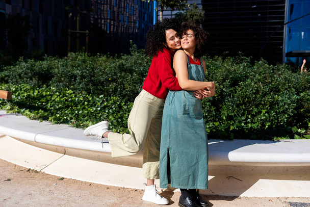 Smiling lesbian couple embracing and relaxing standing outdoors while looking at camera - Φωτογραφία, εικόνα