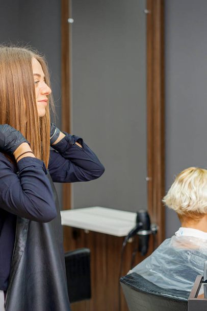 Cabeleireiro feminino coloca um avental preto antes de cortar o cabelo do cliente - Foto, Imagem