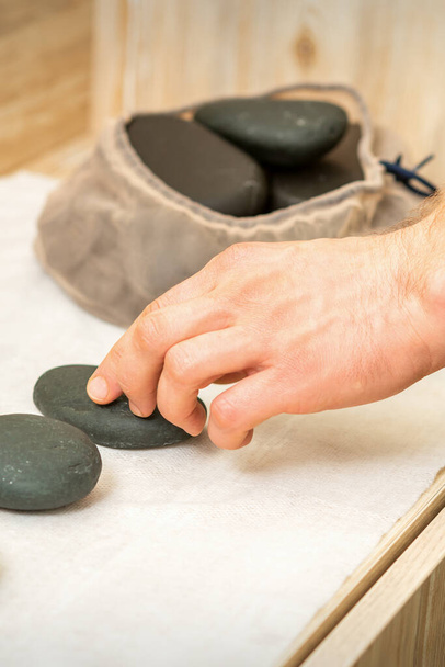 Hand van masseur neemt hete zwarte massage stenen van tafel in spa - Foto, afbeelding