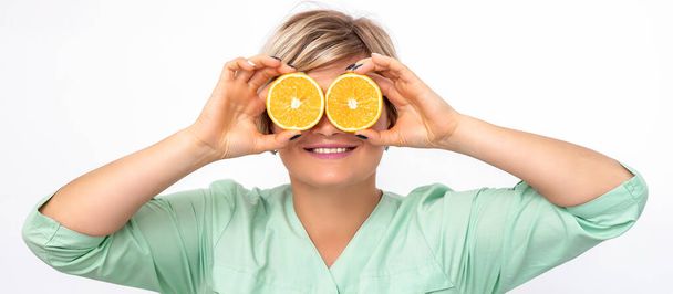 Cosmetologist or nutritionist covering the eyes with two halves orange fruit on a white background - Foto, Bild